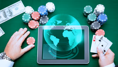 Hands holding poker cards and chips around a tablet displaying a world map